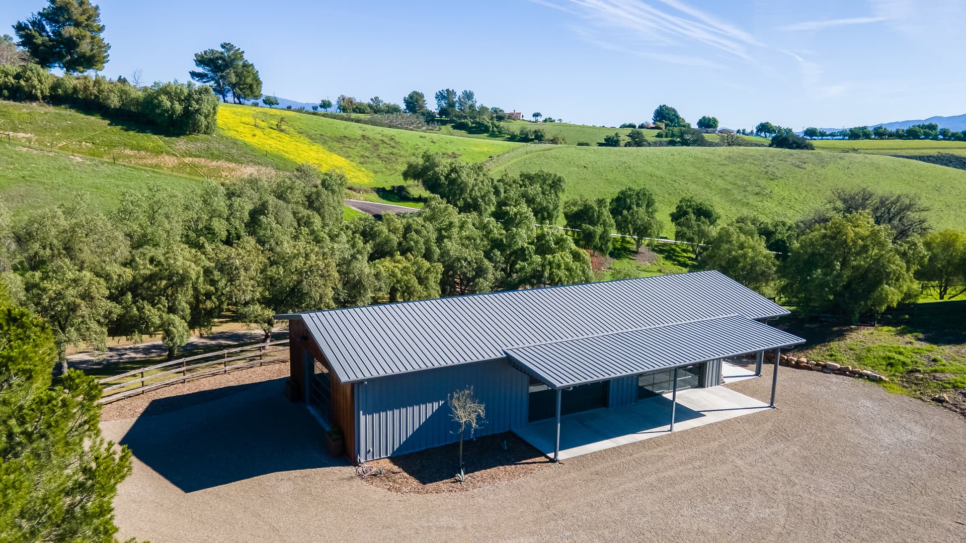 A gray steel building with a covered side canopy among green hills